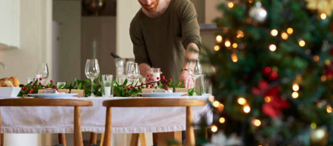 Shot of a young man setting a table for a Christmas party at home